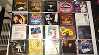 Photo showing 20 various CDs including music and language reference titles arranged on a black surface.