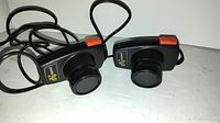 Pair of black Atari 2600 Sears paddle controllers with cords and plugs lying next to each other on a flat surface