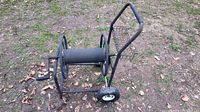 Black metal wagon-style hose reel cart with two back wheels, one front wheel, hand crank, and a small basket attached to the handle. The hose is not included.