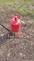 Red Central Pneumatic sandblaster unit outdoors on grass, showing side view of tank with handle and nozzle.