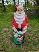 Front view of Empire blow mold Santa Claus standing outdoors on grass, showing filled sack and facial features.