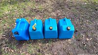 Four blue plastic kerosene tanks arranged side by side on grass, showing black and yellow caps.