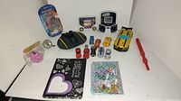 Photo of the lot showing various kids toys on a white surface including cars, electronic game, puzzle, toys, and notebooks.