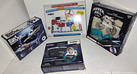 Four boxed toys arranged on a white surface: Orbiter Rocket model, Snap Circuits Jr. kit, Compact Lie Detector game, and Hover Ball helicopter toy.