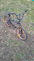 Full view of orange freestyle Kent 30 Chaos FS BMX bike with black frame, orange rims and orange wheel pegs taken outdoors on grass and dirt.