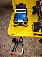 Blue remote control off-road vehicle on yellow plastic container with black and red handheld remote controller.