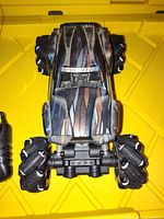 Top view image of camouflage patterned off-road remote control car with large treaded tires on a yellow plastic surface.