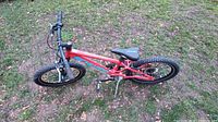 Red Schwinn kids bike lying on grass showing left side and drivetrain.