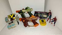 Overview of all items in the vintage toy lot including toy guns, action figures, electronic game, collectible card, and toy vehicle.
