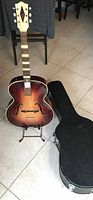 Front view of Hofner archtop acoustic guitar on stand next to black hardshell case.
