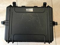 Closed exterior view of the black "MAXIMUM" protective case showing durable plastic with minor scratches.