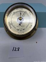 Close-up front view of Royal Mariner brass barometer showing dial face, pressure scale, and weather indicators.