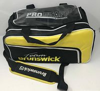 Overall view of the Brunswick black and yellow bowling ball bag with clear plastic lid and branded padded shoulder strap.