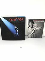 Front view of two coffee table books, one with a black cover showing Mick Jagger under stage lighting, the other with Mick Jagger making a hand gesture, both about The Rolling Stones.