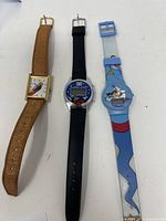 Three Disney-themed watches featuring Rocker Man analog, digital Mickey Mouse, and Aladdin plastic watch with character straps.