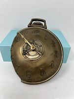 Front angled view of bronze distorted clock with raised numbers and single hand showing antique and artistic design.