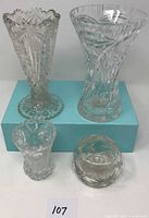Overview photo showing four clear cut glass vases in different shapes and sizes placed on a blue box, highlighting their intricate patterns and clear glass finish.