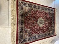 Full view of the rectangular silk floral tapestry rug laid flat, showing red background with floral medallion center and bordered edges with fringes.
