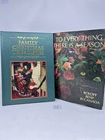 Two large coffee table books shown standing upright: 'Family Christmas Treasures' with green cover and family photo, and 'To Every Thing There is a Season' with seasonal holly cover.