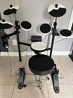 Full view of complete electronic drum set including drum pads, cymbals, foot pedals, and stool with module in center