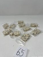 Photo of ten packs of ivory-colored six-sided dice with black dots, each pack sealed in transparent plastic bags.
