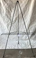 Full view of tall black metal easel with open frame design and three legs standing against a white backdrop.
