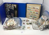 Overview of two stamp albums (blue cover) with various stamps mounted and loose stamps in plastic bags and envelopes.
