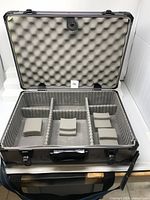 Opened metal hard shell camera lens case showing foam padded interior with adjustable dividers and cushioned inserts.