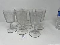Six antique clear glass goblets with a detailed floral and panel pressed pattern visible from the front.