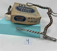 Twisted metal horse bit in front of Victory Racing Plates box with horseshoes inside a white box.