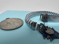 Angle showing front detail of the round Kiwanis Music Festival medal, the double skiff pin with blue enamel, and the linked ID bracelet with pendant.