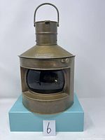 Front view of the antique brass ship lantern showing the green glass lens with the word 'STARBOARD' embossed on the top plate and the curved handle at the top.