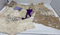 Multiple vintage crochet lace pieces in beige and purple hues displayed on a white background, showing various sizes and patterns including floral embroidery and geometric lace designs.