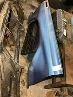 Vintage blue front fender for a 1970s Ford truck shown lying on the ground next to other vehicle parts.