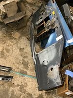 Wide-angle shot of the steel radiator support panel laid flat on a concrete floor showing structural design and rust on brackets.