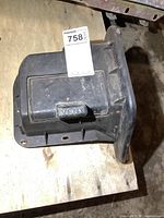 Top view of black plastic floor vent showing vent flap marked 'VENT' with attached label.