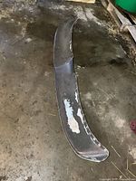 Overall view of the curved metal visor showing wear and paint peeling, sitting on a concrete surface.