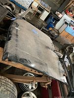 Full top angled view of the black Chevrolet S10 truck hood showing surface condition and some rust on underlying stand.