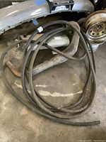Two lengths of black rubber Goodyear hoses coiled on a concrete floor, one with a curved fitting attached.