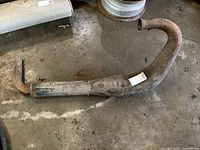 Full side view of the steel 2 stroke exhaust muffler and pipe, showing overall length and condition including rust and wear.