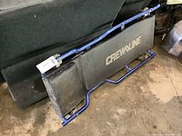 Full view of aluminum frame shop creeper with black padded cushions and visible 'CREWLINE' branding on cushion, showing some wear.