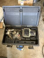 Wide view of the open carrying case showing the exhaust analyzer main unit along with bundled cables and accessories stored in labeled compartments.