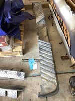 Side angled view of the used metal rear bumper with step tread pattern and integrated park sensor hole visible.