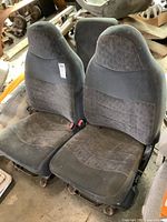 Photo showing pair of dark gray Ford truck bucket seats placed on the floor with visible wear and dirt.