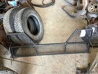 Black metal 5th wheel tailgate for GM truck sitting on the floor near tires and automotive parts.