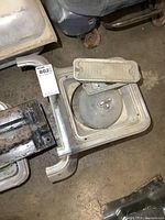 Pair of vintage GM truck light bezels showing one round headlight and one rectangular signal light bezel from a top perspective on the floor.