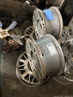 Set of four GM aluminum mag wheels stacked on a floor showing geometric spoke design and usage wear.