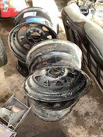 Four stacked GM steel wheels painted black, showing usage wear.