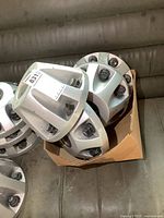 Four silver 8 bolt GMC centre caps stacked in a cardboard box on a dark surface.