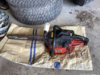 Full view of the Jonsered chainsaw laid on paper with tires in the background, showing the cutting bar and chain.